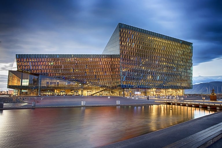 Contemporary glass building with unique angular design at dusk, reflecting city lights.