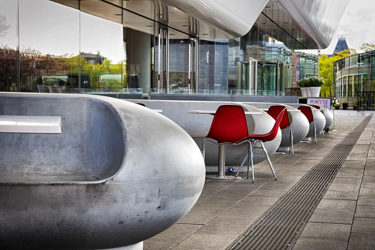 Contemporary outdoor seating with concrete benches and vibrant red chairs at a modern building.