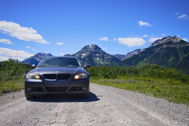 Car parked on a gravel road with majestic mountains and blue sky in the background.