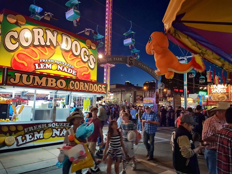 Corn Dogs fairground food stand illuminated at night with colorful signage and a lively crowd.