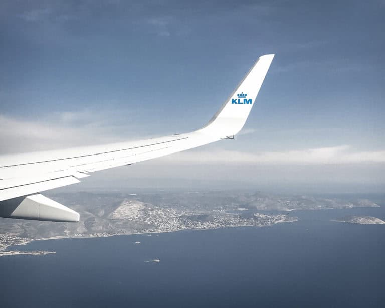 KLM airplane wing view over coastal city and ocean from above.